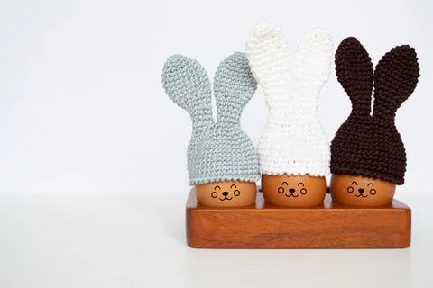 Knitted Easter eggs with bunny ears hats in a wooden stand on a white table. Stock Photos