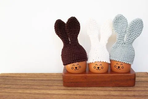 Knitted Easter eggs with bunny ears hats in a wooden stand on a wooden table. Stock Photos