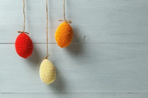 Knitted Easter eggs on strings. On a light wooden background, horizontal with Stock Photos