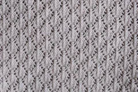 Knitted fabric with symmetrical lace pattern in light grey color. Close-up te Stock Photos