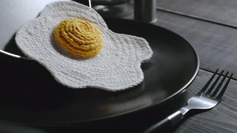 Knitted fried eggs being put in a plate. Synthetic food. Dark wooden surface Stock Footage 140626692