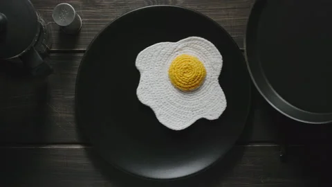 Knitted fried eggs being put in a plate. Synthetic food. Dark wooden surface Stock Footage 140626695