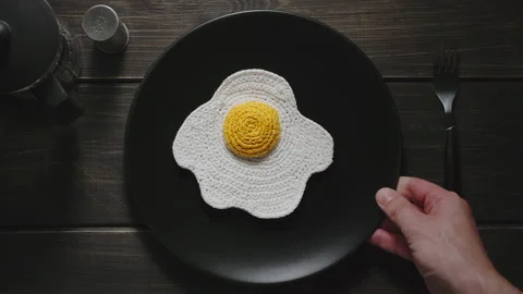 Knitted fried eggs in a plate putted on a table. Dark wooden surface Stock Footage 140626701