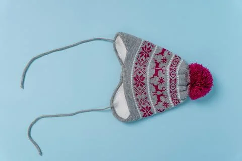Knitted hat with ear flaps, pattern, and pom pom on light blue background Фото