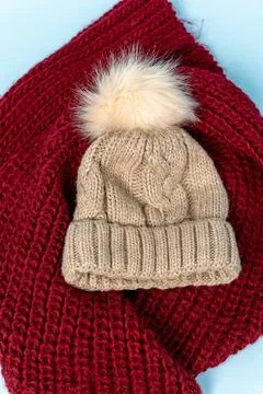 Knitted hat with pom pom placed on a red textured scarf Stock Photos
