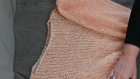 Knitted peach shawl held by hands, soft wool fabric texture, light orange yar Stock Footage 334753085