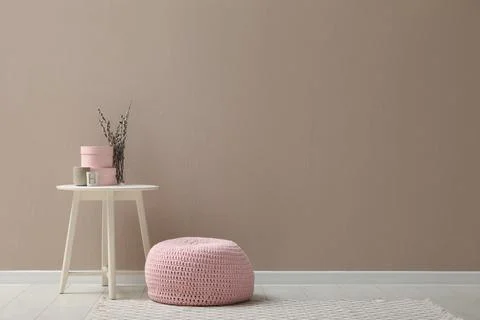 Knitted pouf and decor elements near beige wall indoors. Space for text Stock Photos