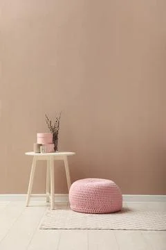 Knitted pouf and decor elements near beige wall indoors. Space for text Stock Photos