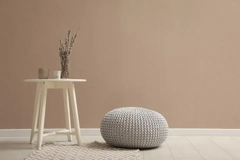 Knitted pouf and decor elements near beige wall indoors. Space for text Stock Photos
