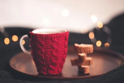 Knitted red cup of tea with stack of homemade cookies on wooden tray in kitch Stock Photos