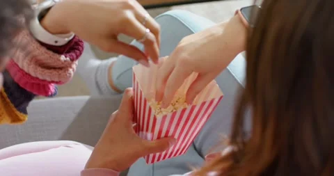Knitter is pausing knitting, grabbing popcorn from striped popcorn box to share Stock Footage 341467513