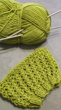 Knitting pattern using thick green yarn. Needles, thread, and green fabric Фото