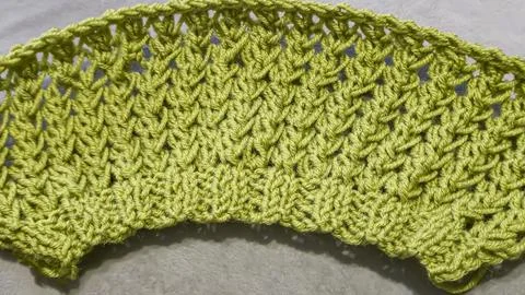 Knitting pattern using thick green yarn. Needles, thread, and green fabric Foto stock