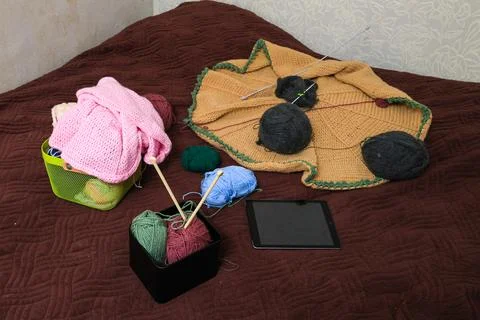 Knitting project in progress with yarn balls, needles, and tablet on a bed Stock Photos