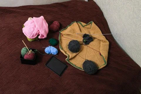 Knitting project in progress with yarn balls and tablet on a textured bedspre Stock Photos