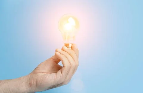 Knowledge and idea concept. Light bulb with light in hand on a blank blue Stock Photos