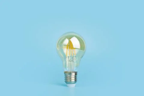 Knowledge and idea concept. Light bulb with light on a blank blue background. Stock Photos