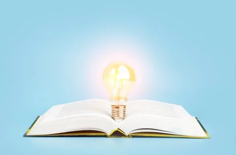 Knowledge study learning concept. Open book with a glowing light bulb on a blue Foto stock