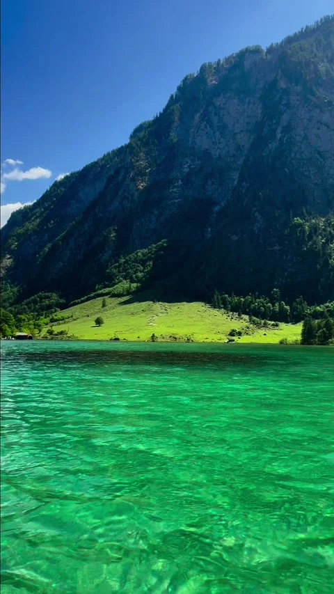 Koenigssee emerald clear water below steep cliffs and green meadow 動画素材 341769002