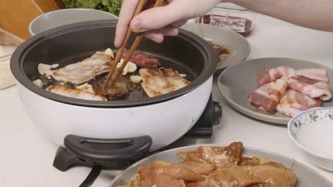 Korean barbecue at home dining with friend cooking meat on grill flipping Stock Footage