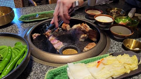 Korean BBQ Pork Belly Grilling on Tabletop Grill with Vegetables and Side Dishes Stock Footage 332046006