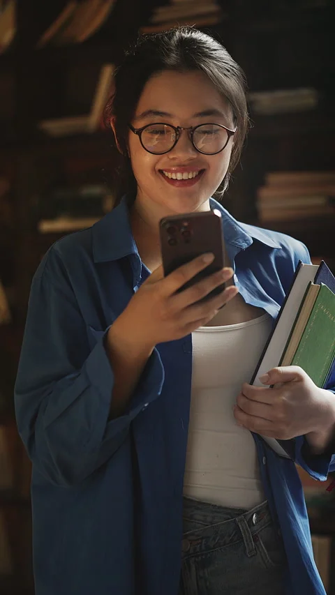 Korean female student choosing e-book instead of paper book, typing on phone Stock Footage 331884366
