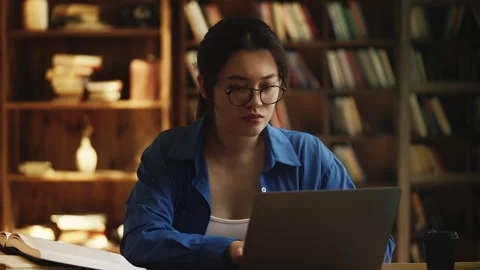 Korean female student does research in a library, types on laptop, reads a book Stock Footage 331876869