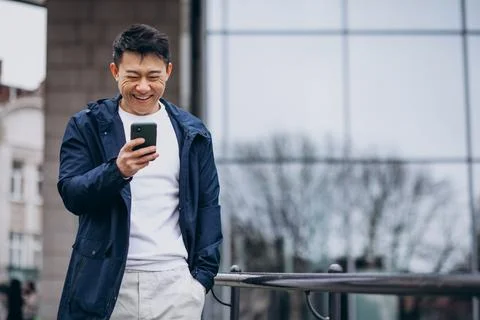 Korean guy using phone outside thes treet Stock Photos