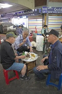 Korean men sit on plastic stools and eat at Gwangjang Market traditional street Stock Photos