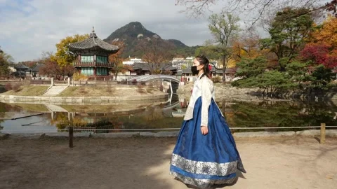 Korean woman in Hanbok walking in Seoul Palace w/ lake, pagoda & mountain Stock Footage