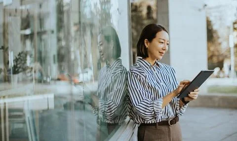 Korean woman using a tablet while standing outside a modern building in the.. Stockfoto's