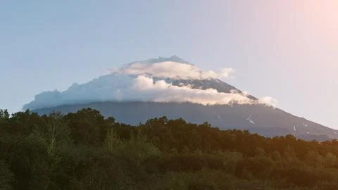 Koryaksky volcano with cloud cap above forest at sunrise, Kamchatka view Stock Photos
