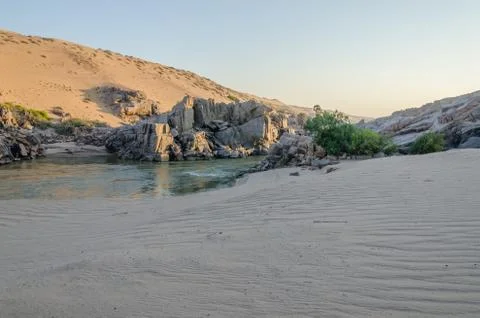 Kunene River in front of towering ancient Namib Desert sand dunes Stock Photos