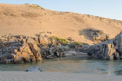 Kunene River in front of towering ancient Namib Desert sand dunes 写真素材
