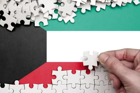 Kuwait flag  is depicted on a table on which the human hand folds a puzzle of Foto stock