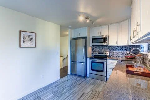 L-shape kitchen room design with white cabinets, brown granite countertops, m Stock Photos