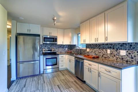 L-shape kitchen room design with white cabinets, brown granite countertops, m Stock Photos
