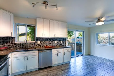 L-shape kitchen room design with white cabinets, brown granite countertops, m Stock Photos