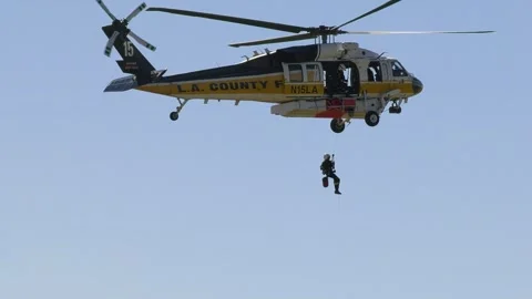 LA county helicopter dropping a rescue fighter to the ground, in sunny Stock Footage 243176753