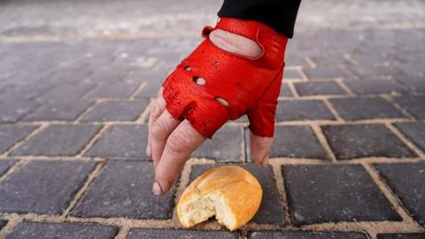 La mano con un guante rojo puesto, está tomando el pan del suelo Stock Photos