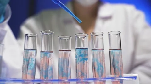 Lab assistant adding blue liquid in test tube, monitoring chemical reaction. Stock Footage 141842546