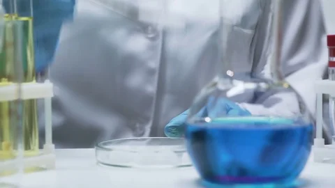 Lab assistant adding dry ice into flask with bright blue mixture causing bubbles Stock Footage 73750421