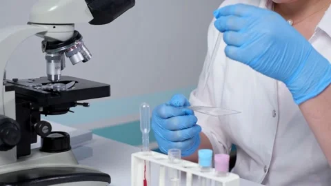 Lab assistant drips transparent liquid on slide at table Stock Footage 156277377
