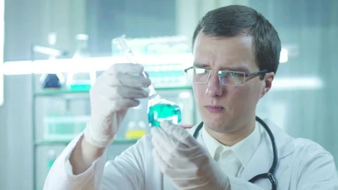 The lab assistant looks at the blue liquid in the flask Stockbeeldmateriaal 82973759