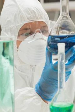 Lab assistant with mask looking at blue liquid Stockfoto's