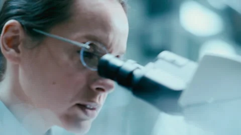 Lab Assistant Taking Notes as Female Scientist Working with Microscope Stock Footage 331337772