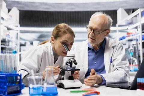 Lab manager teaches intern to check product surface for defects using microscope Stock Photos