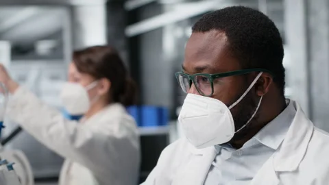 Lab scientist removing protective face mask to scratch beard while using PC Stock Footage 320145168