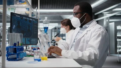 Lab scientist removing protective face mask to scratch beard while using PC Stock Footage 320147121
