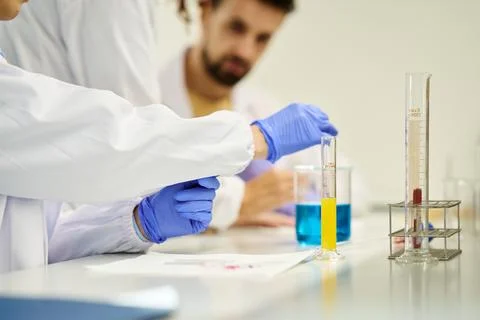 Lab team comparing colored liquids in graduated cylinders Photos
